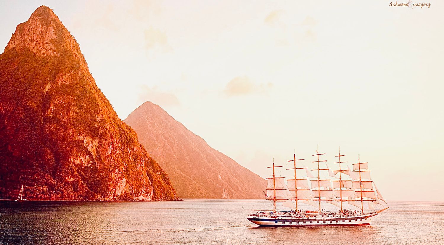 Sailing ship with five masts passing by dramatic pita mountain peaks at sunset in St Lucia by ASHWOOD studios