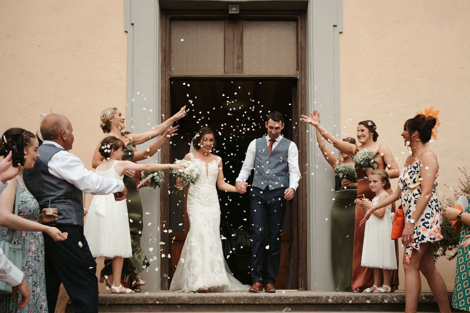 Wedding party celebrating with confetti outside a building.