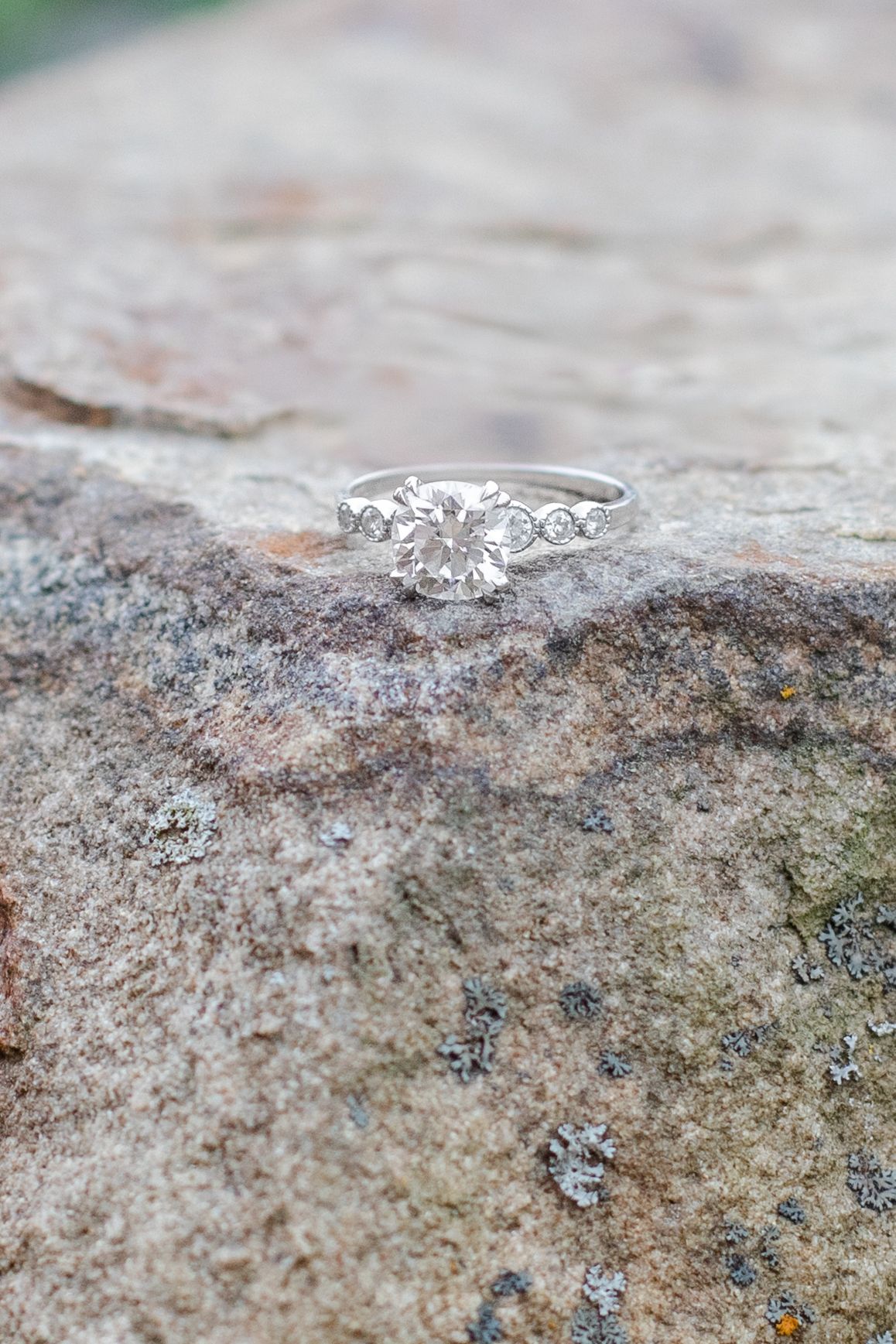 Delicate silver engagement ring with diamond details photographed on textured stone surface.
