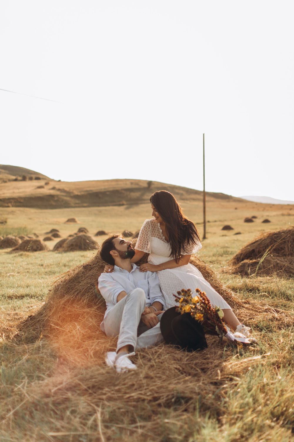Romantic sunset portrait in a rustic field with sunflowers and rolling hills.