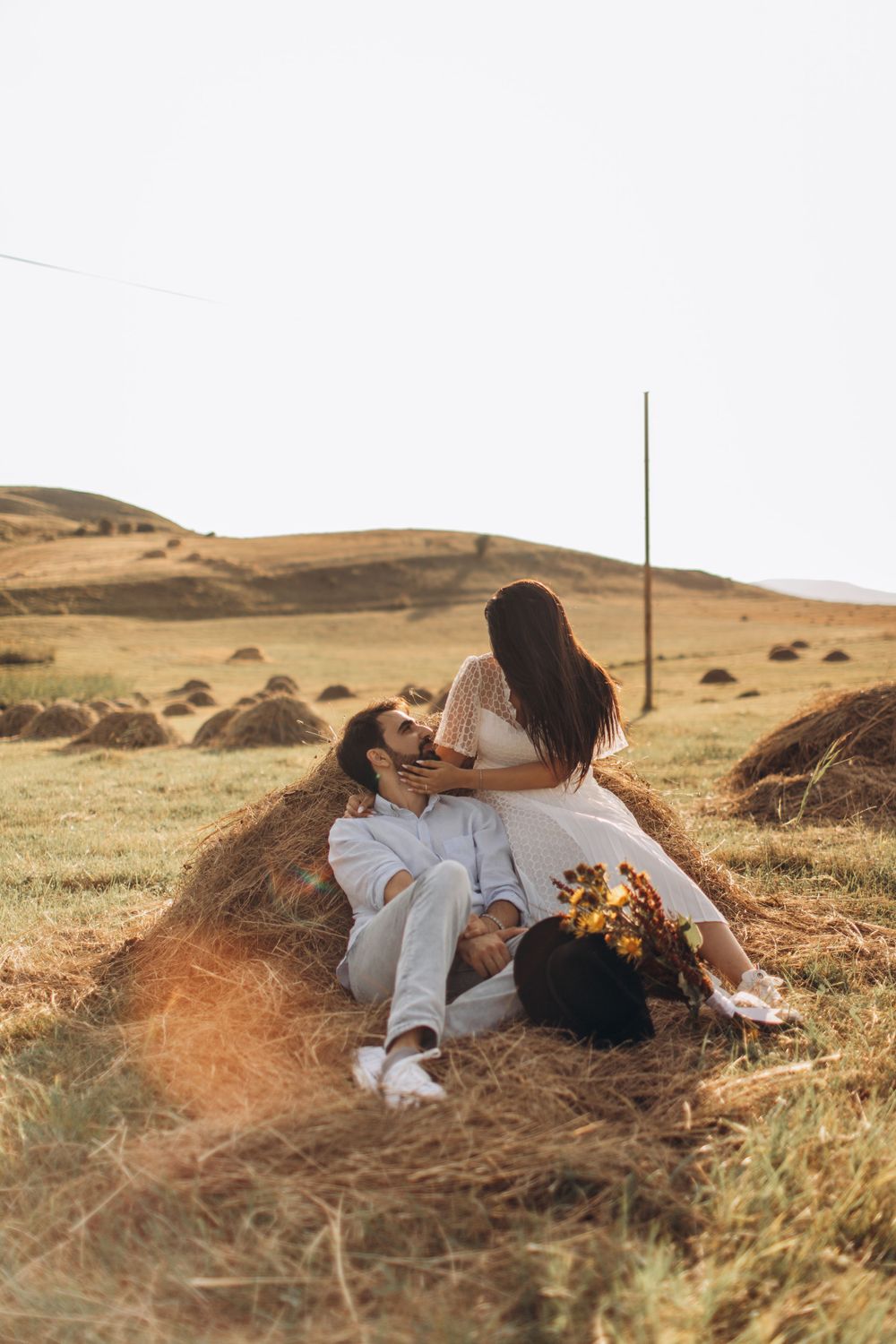 Romantic countryside portrait with couple on hay bale at golden hour.