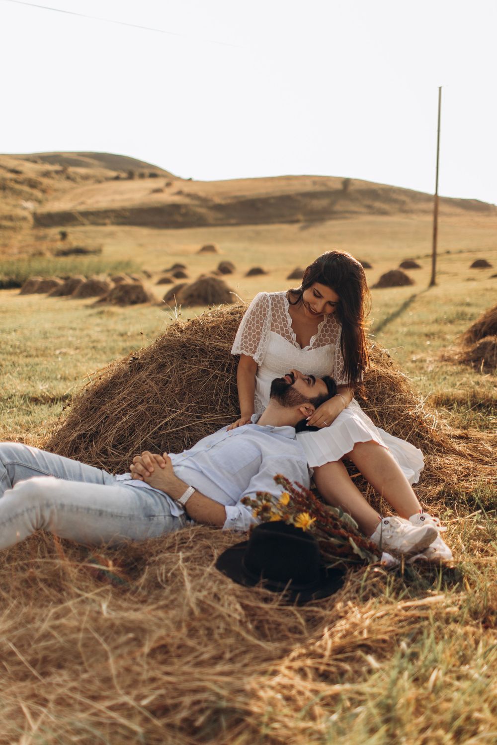 Intimate moment captured between couple lounging on hay bales in rural countryside.