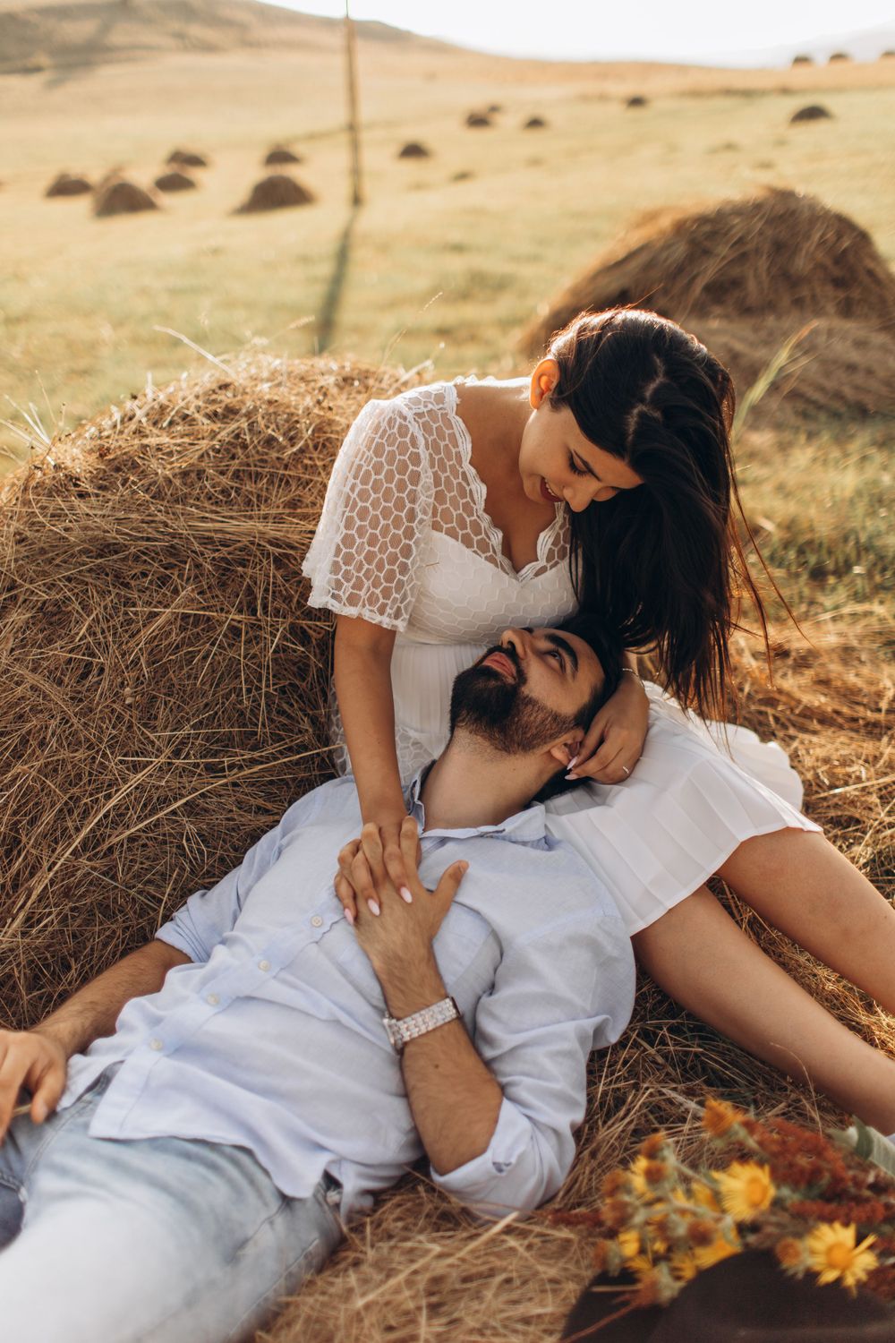 Sweet countryside engagement photo of couple embracing by hay bale at golden hour.
