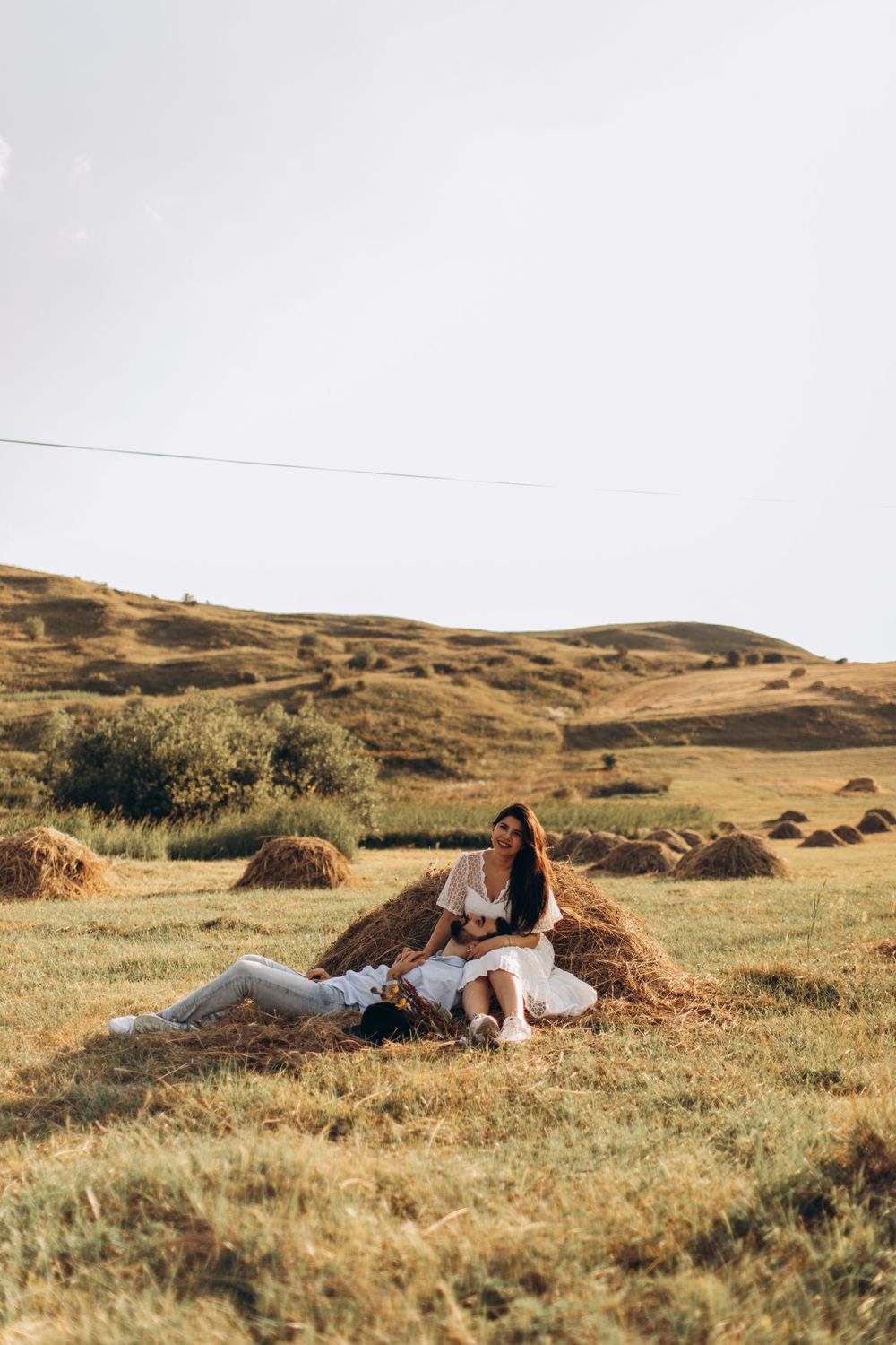 Romantic outdoor portrait of couple relaxing by hay bales in pastoral landscape.