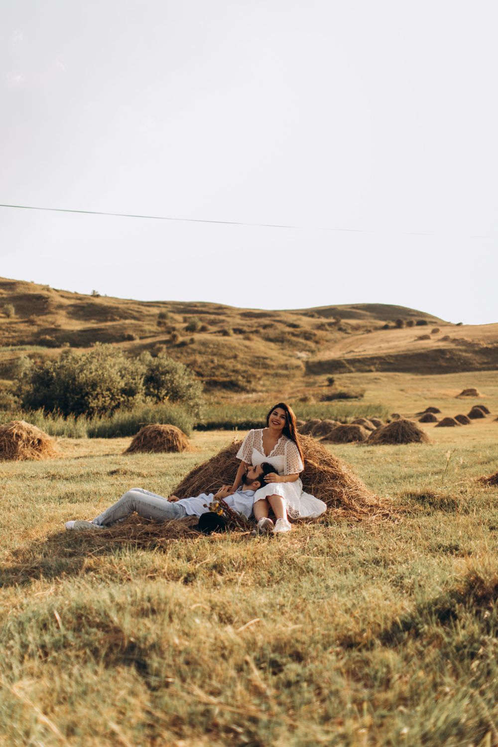 Dreamy countryside photoshoot with couple lounging against rustic hay bale.