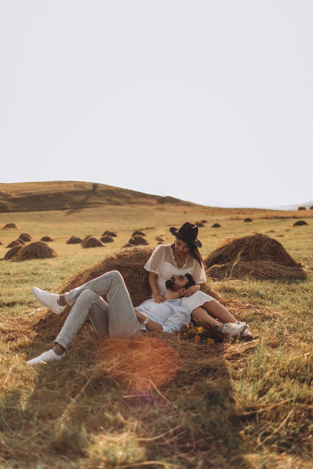Casual countryside photo session featuring couple's intimate moment by hay bale.