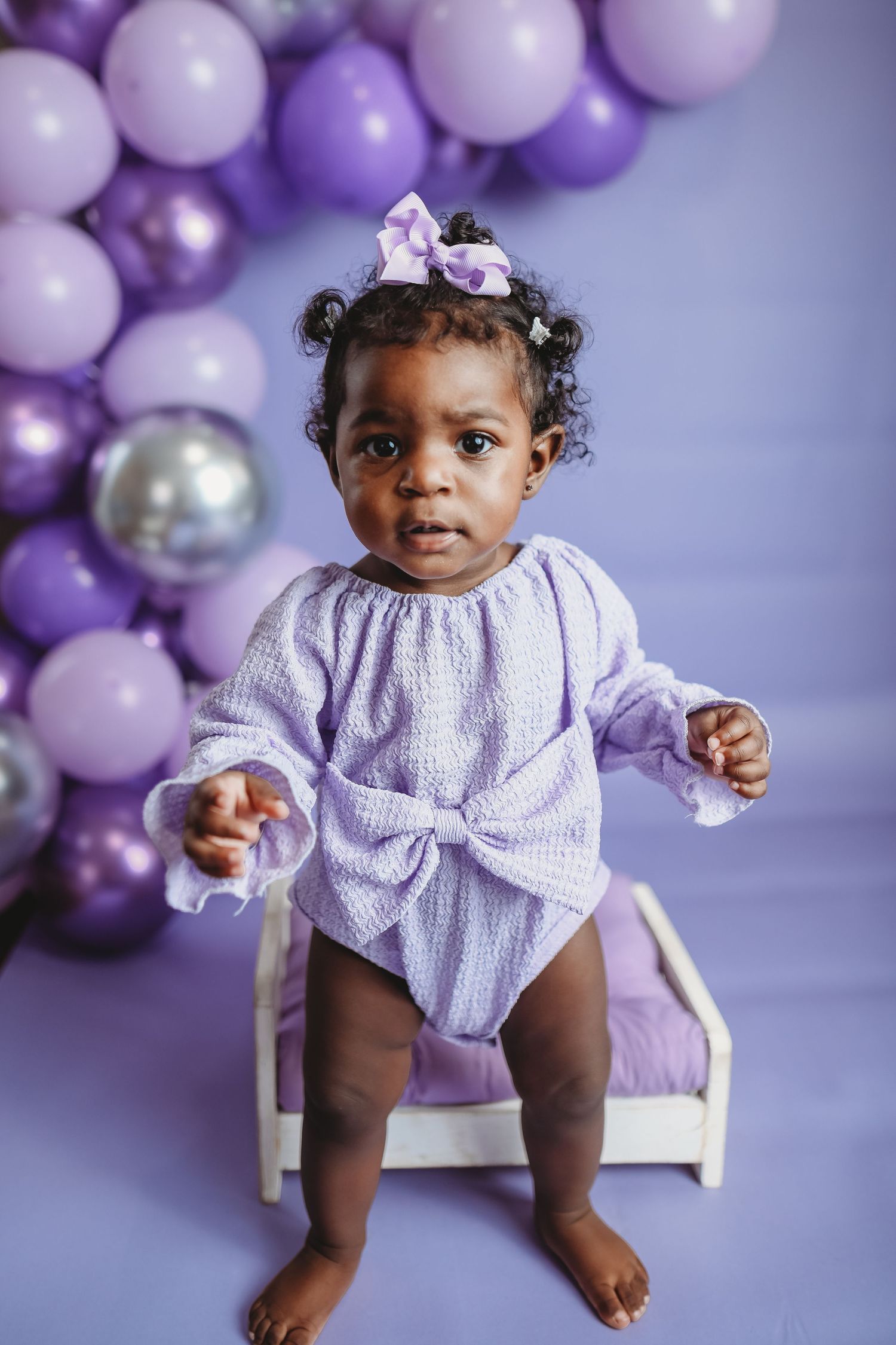Purple themed portrait with balloon arch and lavender outfit creating dreamy setting.