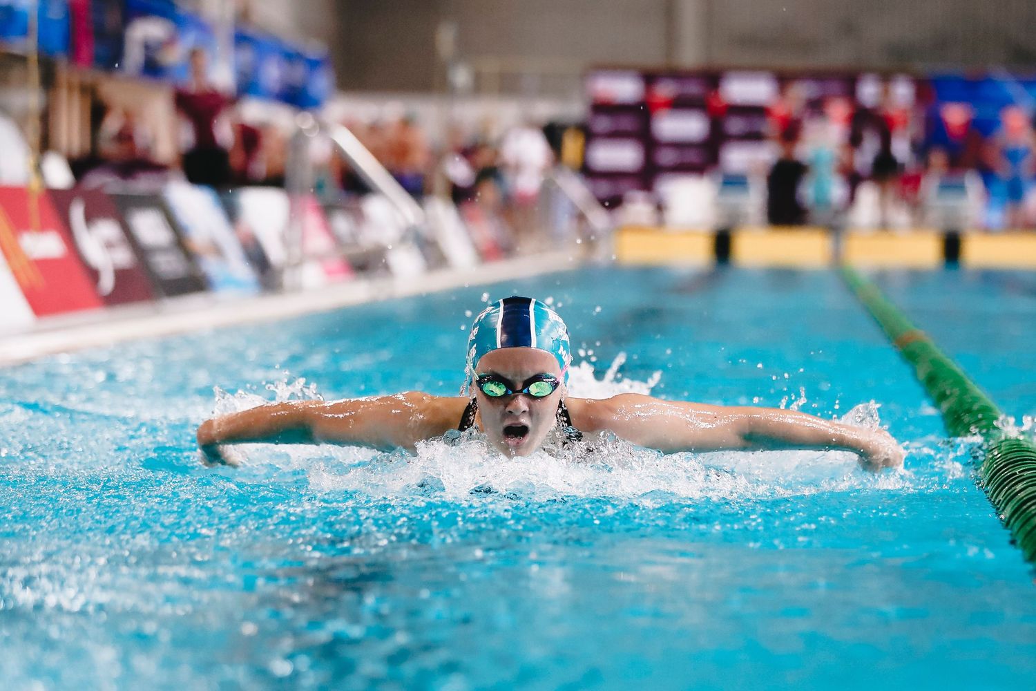 Swimmer performing butterfly stroke in competition pool with water splashing.