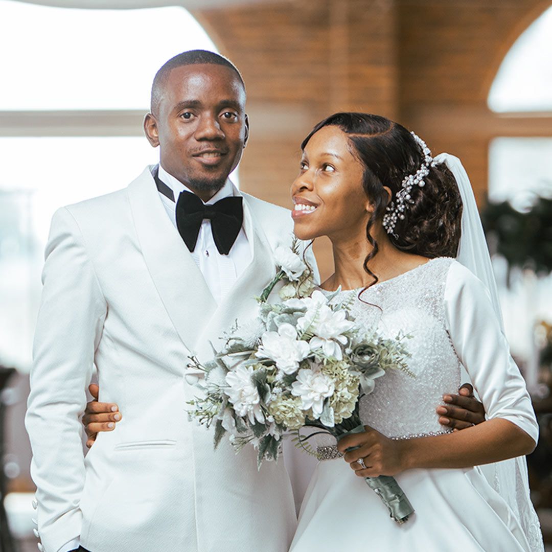 A bride and groom share a joyful moment on their wedding day, the bride holding a white and green bouquet.