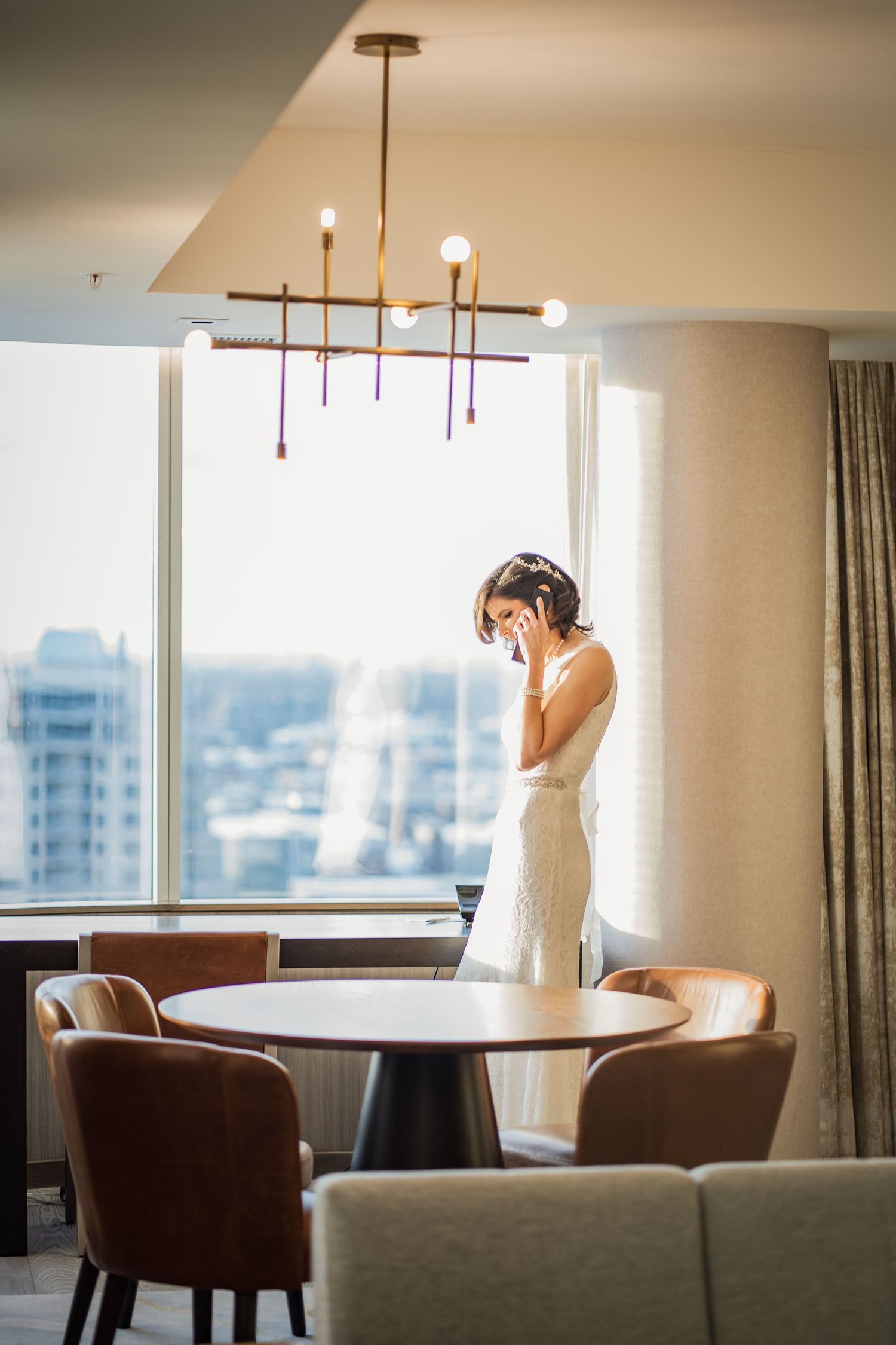 Elegant scene of person in white dress standing by window in modern room with unique chandelier.