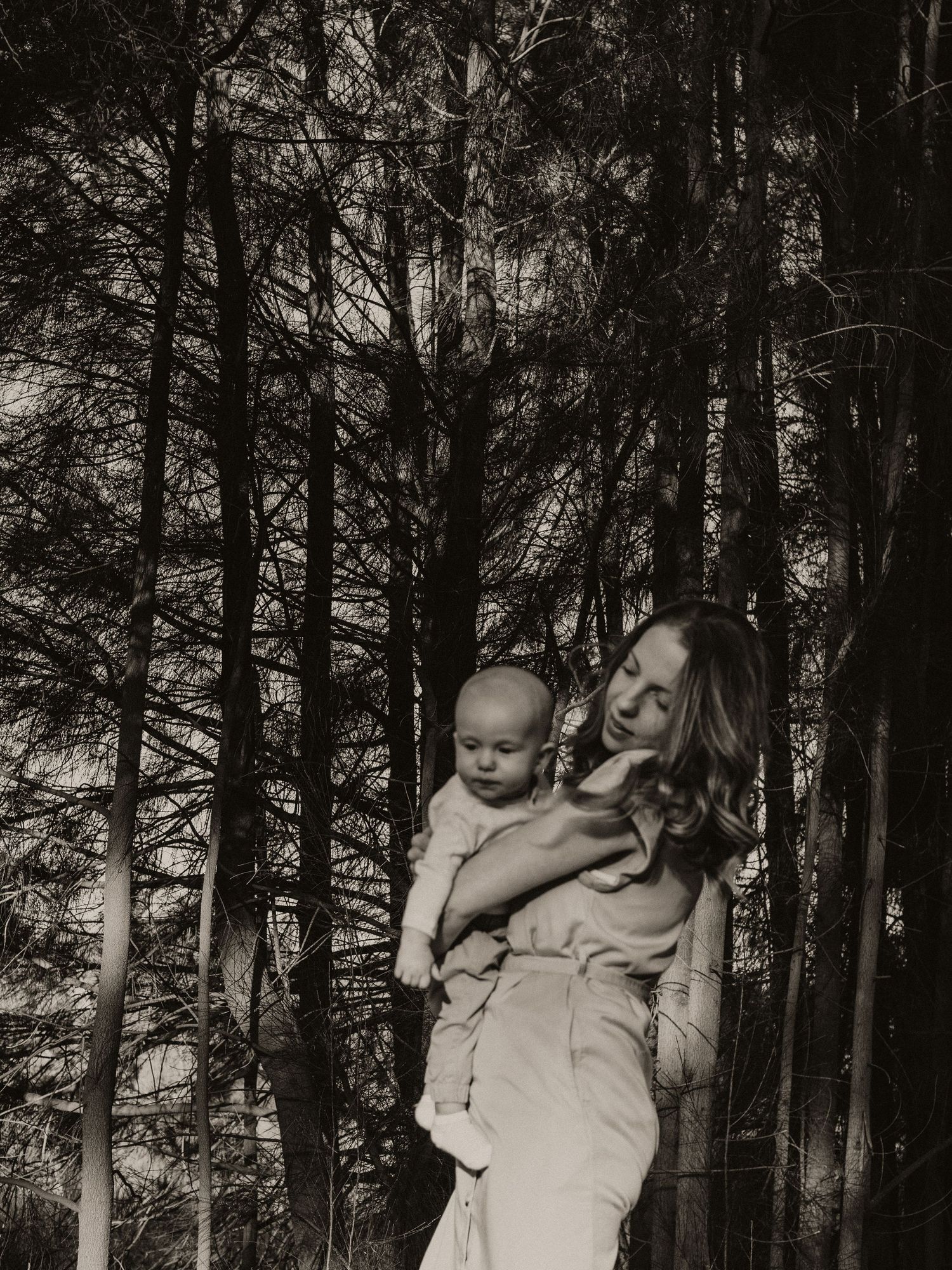 Mother holding her newborn baby boy in her arms in front of trees