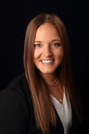 Professional studio portrait of person in black blazer and white top against dark background.