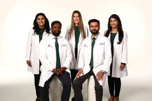 Group of medical professionals wearing white coats and green ties posing against white background.