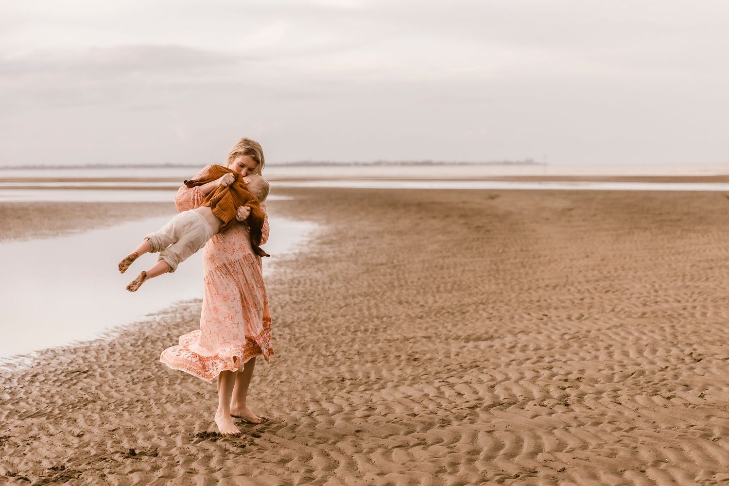 Mother swinging around her toddler son during a family photo shoot at Nudgee Beach in Brisbane