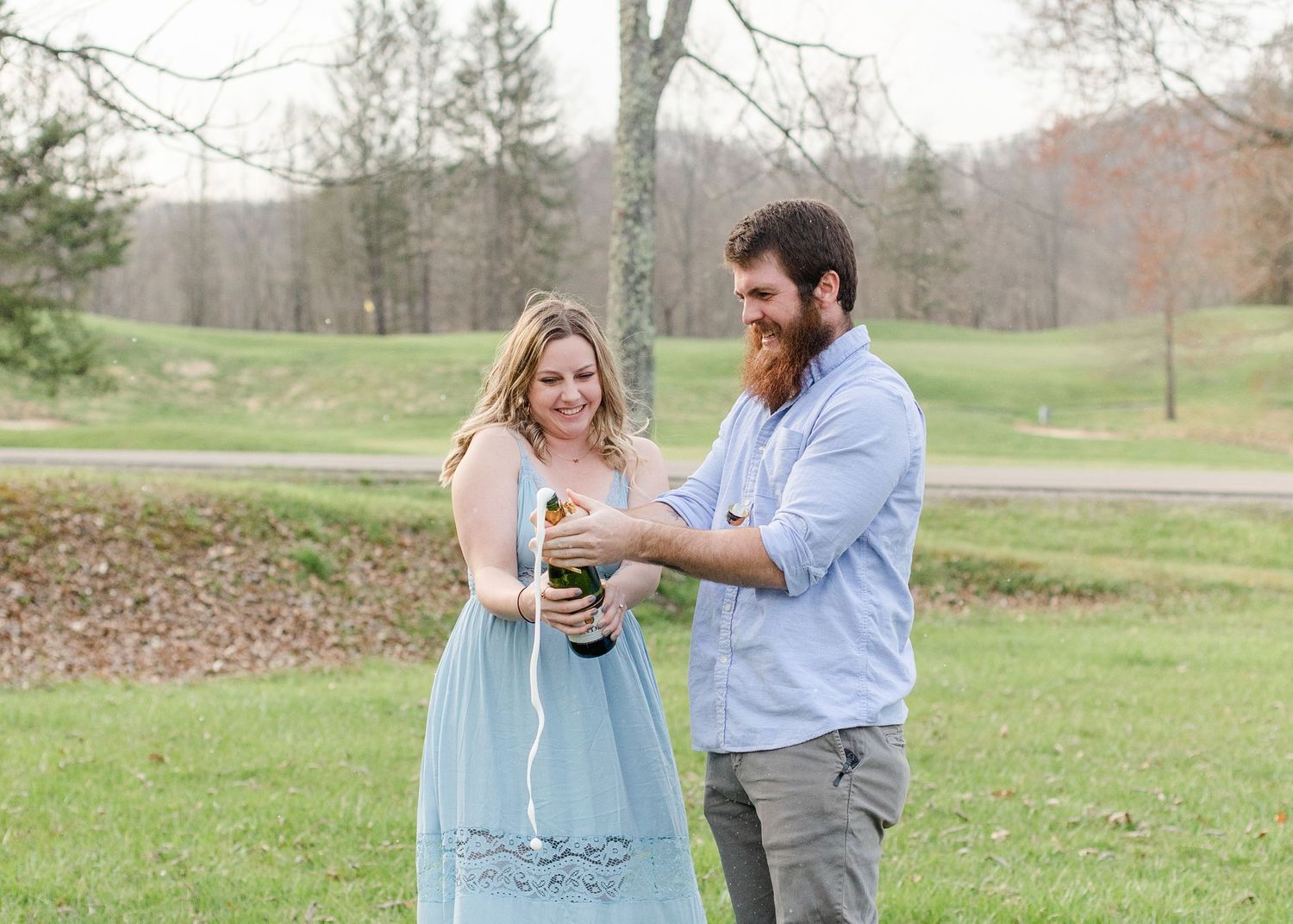 A couple embraces in a sunlit park setting during a spring engagement photoshoot.