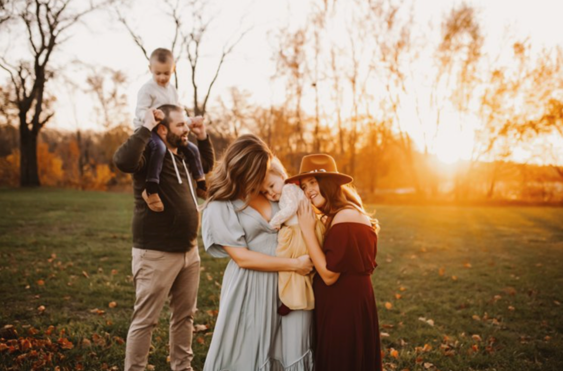 A couple embraces during golden hour sunset in a park with autumn leaves scattered on the ground.
