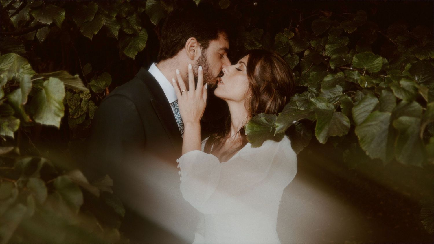 A romantic couple sharing an intimate moment among green foliage at dusk.