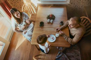 Family gathering around wooden dining table for mealtime in sunlit kitchen.
