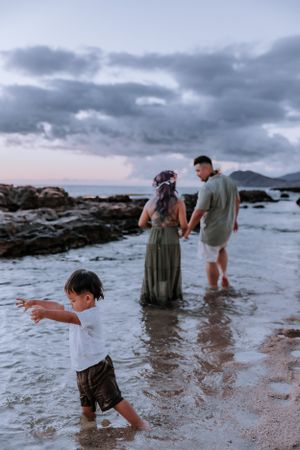 Family playing in shallow ocean water at sunset with rocky coastline visible.