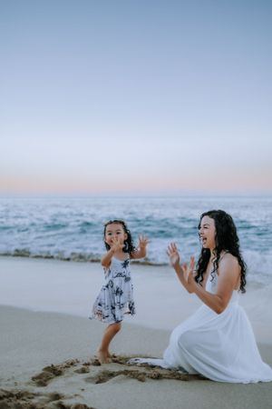 Two people sharing joyful moments while sitting on a sandy beach at dusk.
