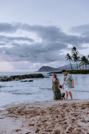 People enjoying a scenic beach at sunset with palm trees and mountains in the background.