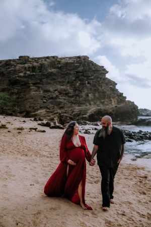 A couple poses together on a scenic beach with dramatic rocky cliffs in the background.