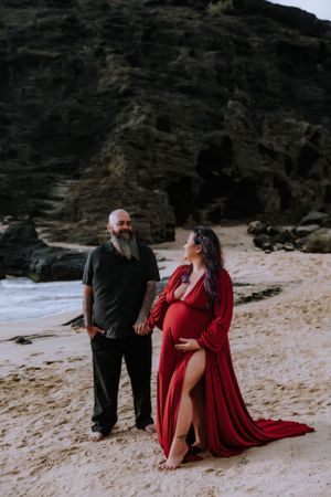 Two people share an intimate moment on a sandy beach with dark cliffs behind them.