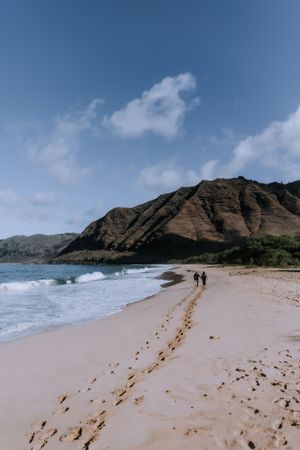 Footprints trail along sandy beach with dramatic mountain coastline in background.