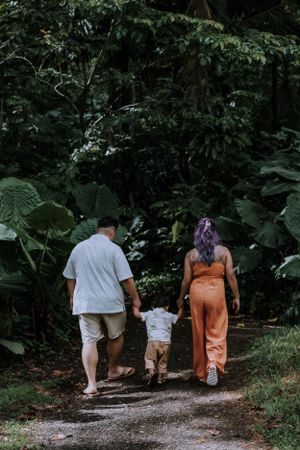 A family walks together on a wooded nature trail surrounded by lush greenery.