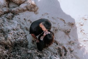 Intimate moment captured between couple on rocky beach during photo session.