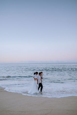 A couple walks along the shoreline during sunset at a serene beach.