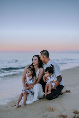 A family sharing intimate moments while sitting together on a sandy beach at dusk.