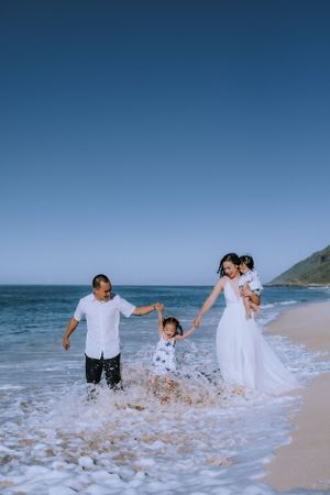 Newlyweds splash through ocean waves together on a beach during their wedding photo session.