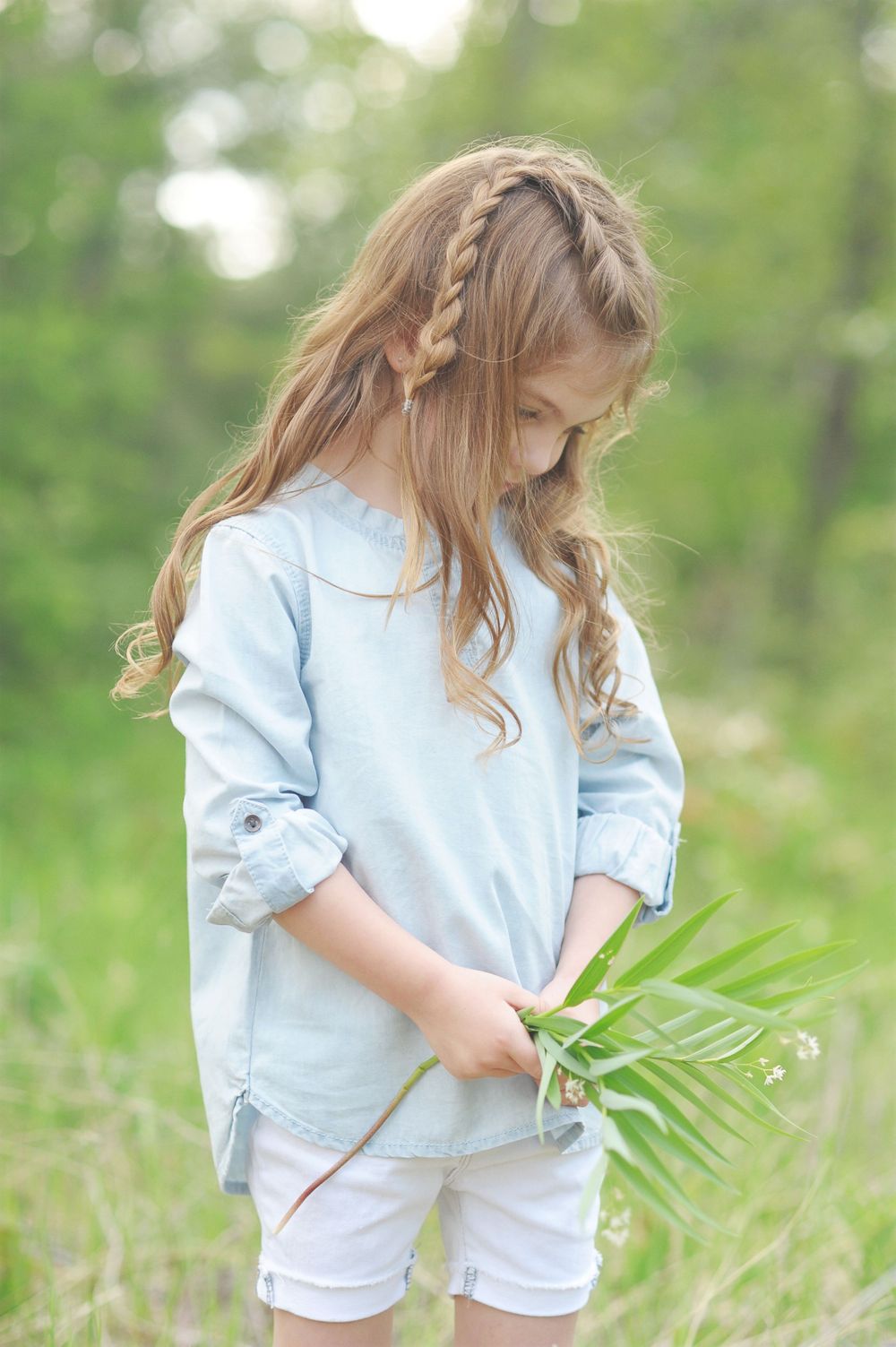 A young child with braided hair holds a palm frond while wearing a light blue shirt.