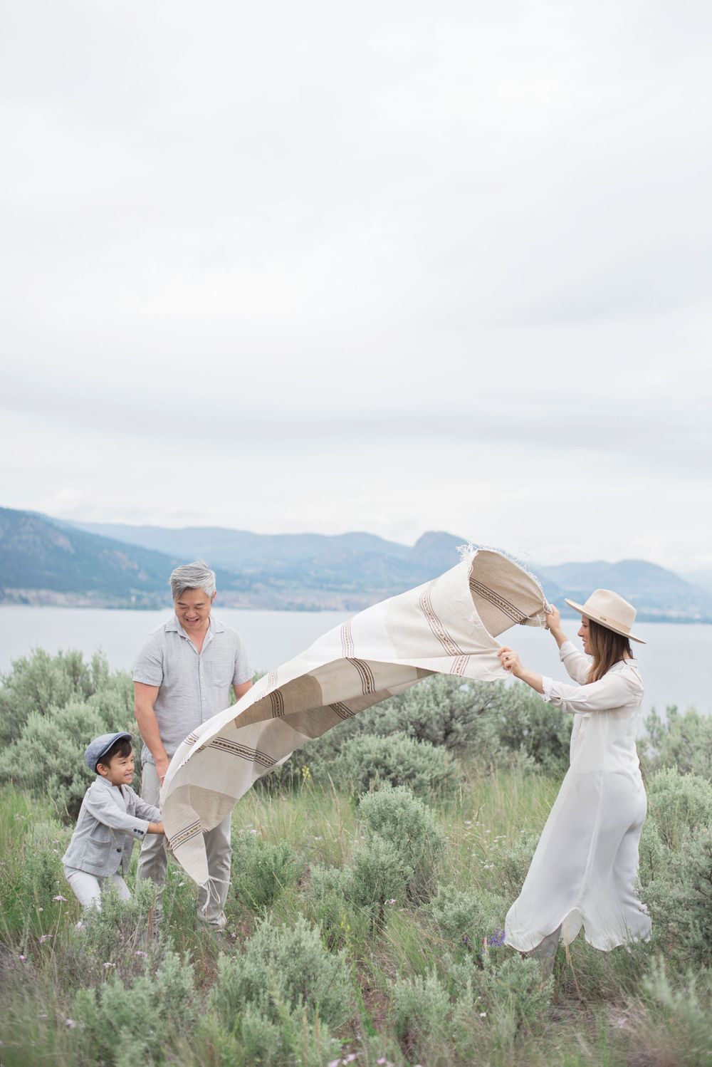 Family playing with a flowing white blanket against a mountainous lakeside landscape at Penticton, B.C.