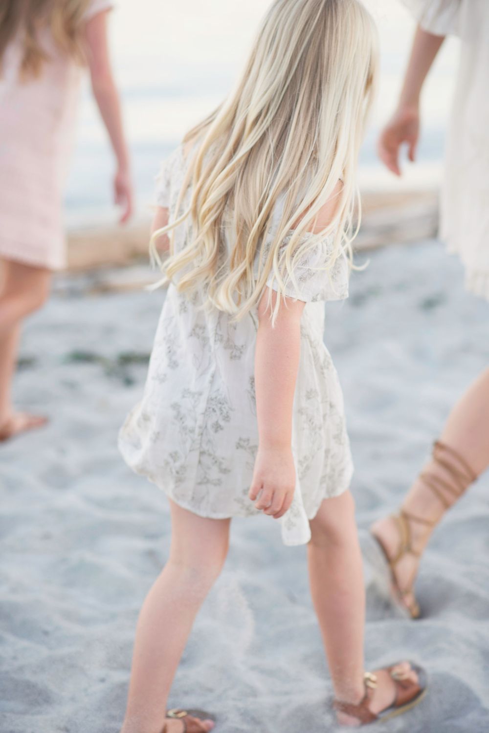 A child in a white floral dress walks on sandy beach in Victoria, B.C.