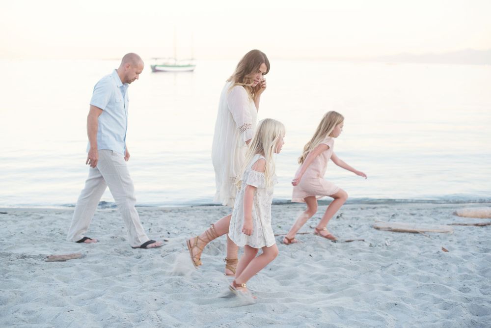 A family taking a casual stroll together on a white sandy beach at sunset in Victoria, B.C.