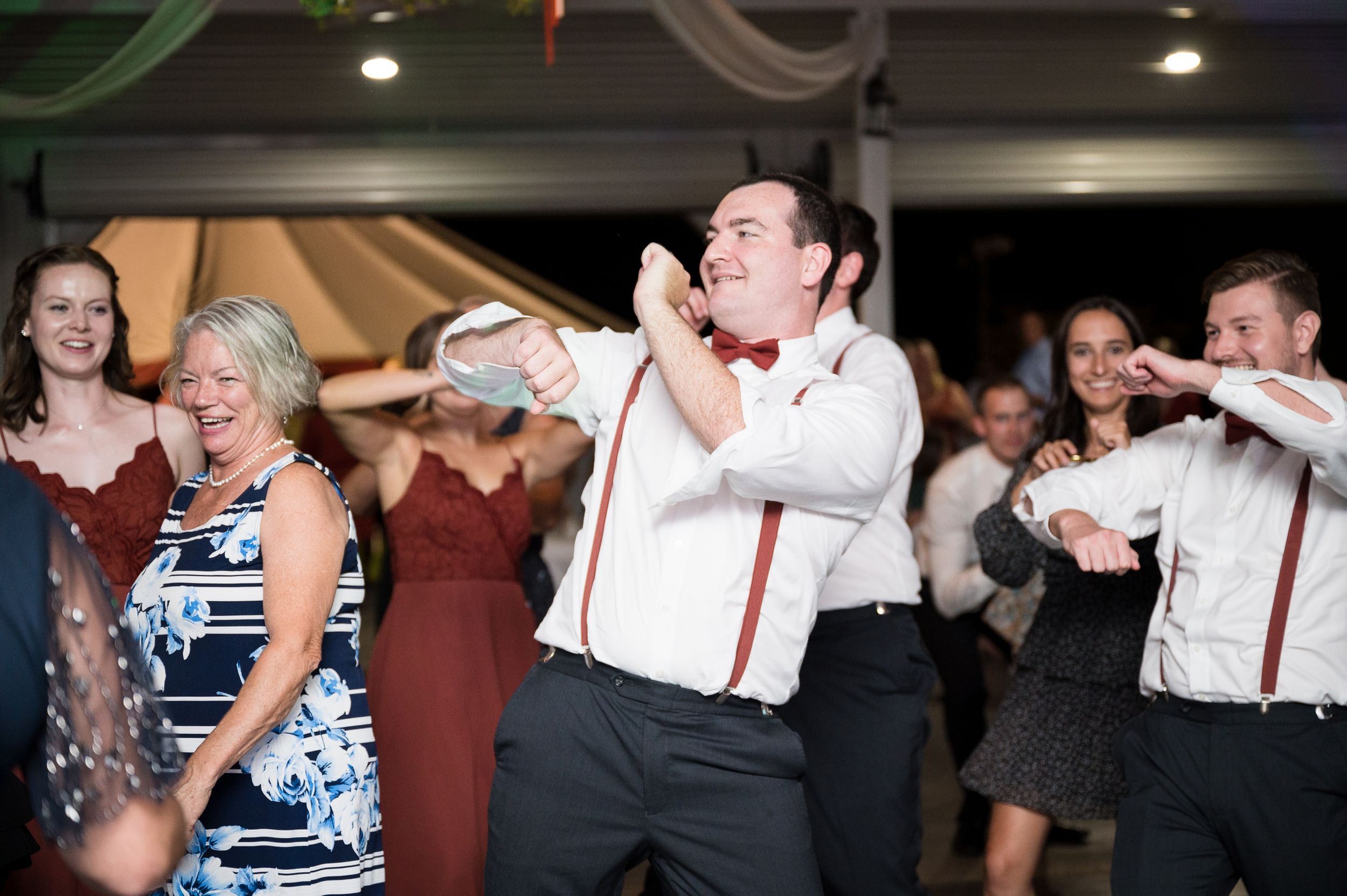 Wedding reception guests dancing energetically on the dance floor with suspenders and party attire.
