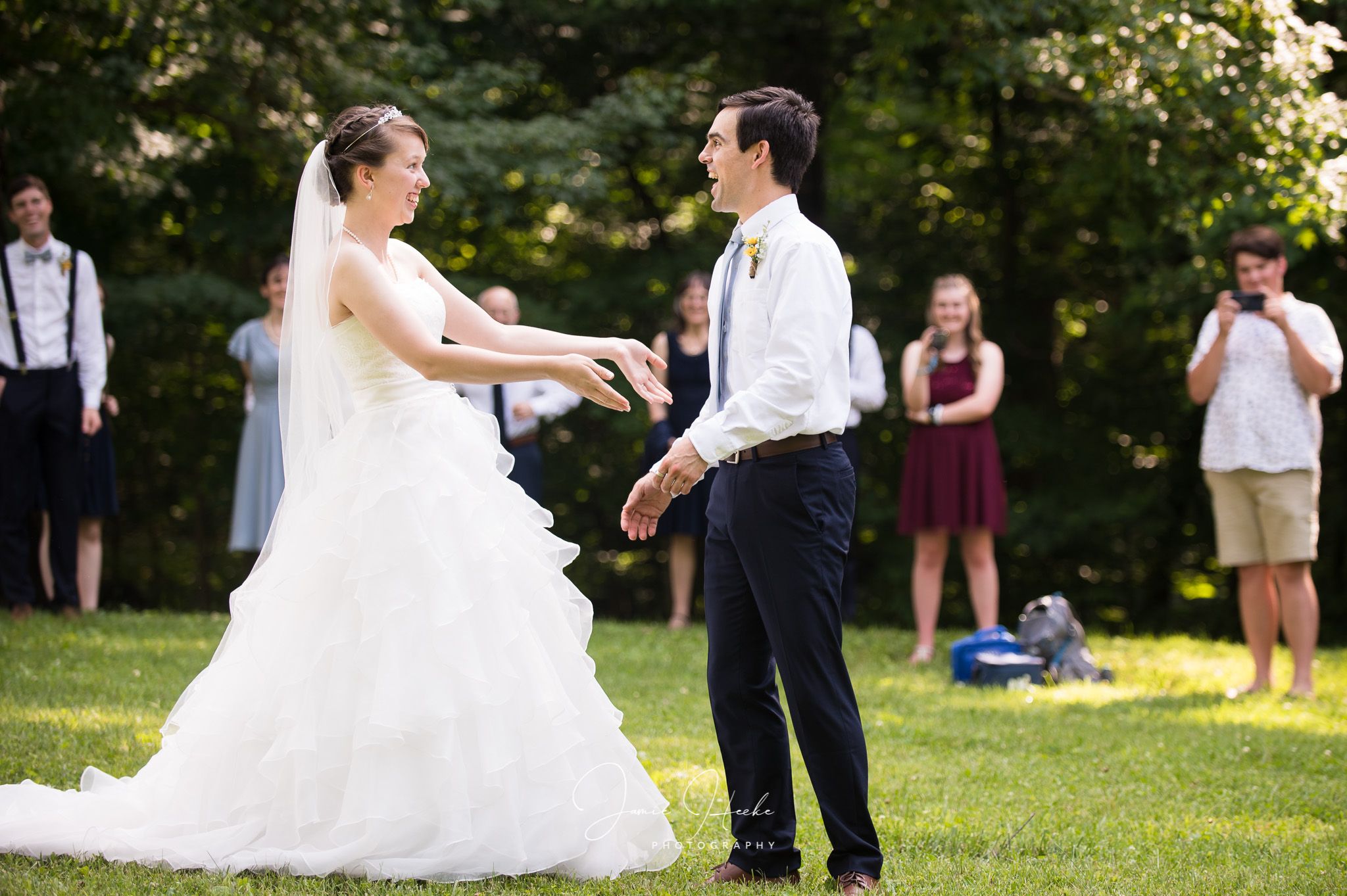 A couple shares a playful moment during their outdoor wedding ceremony on a grassy lawn.