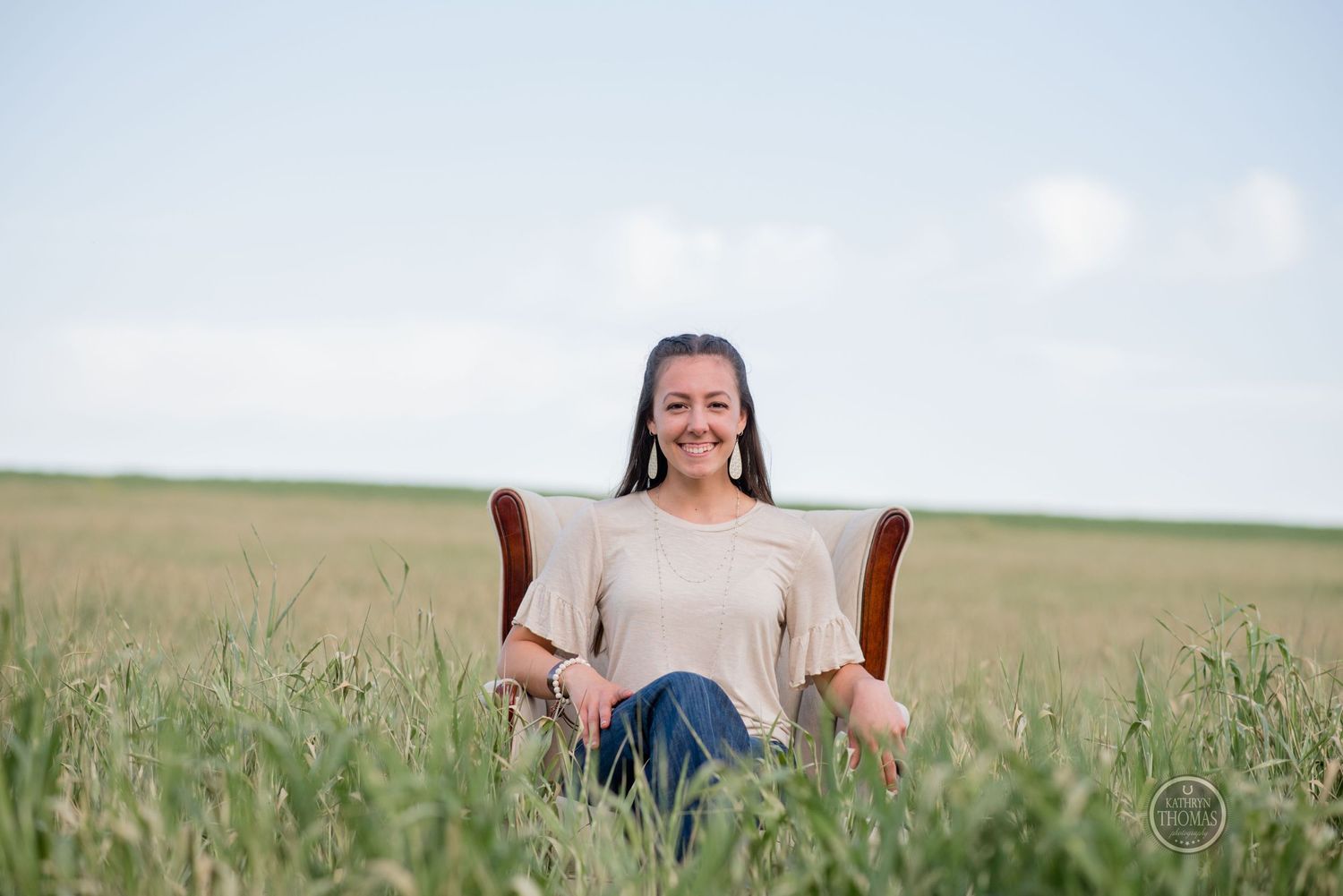 A vintage armchair sits in tall grass with someone relaxing in a casual outfit.