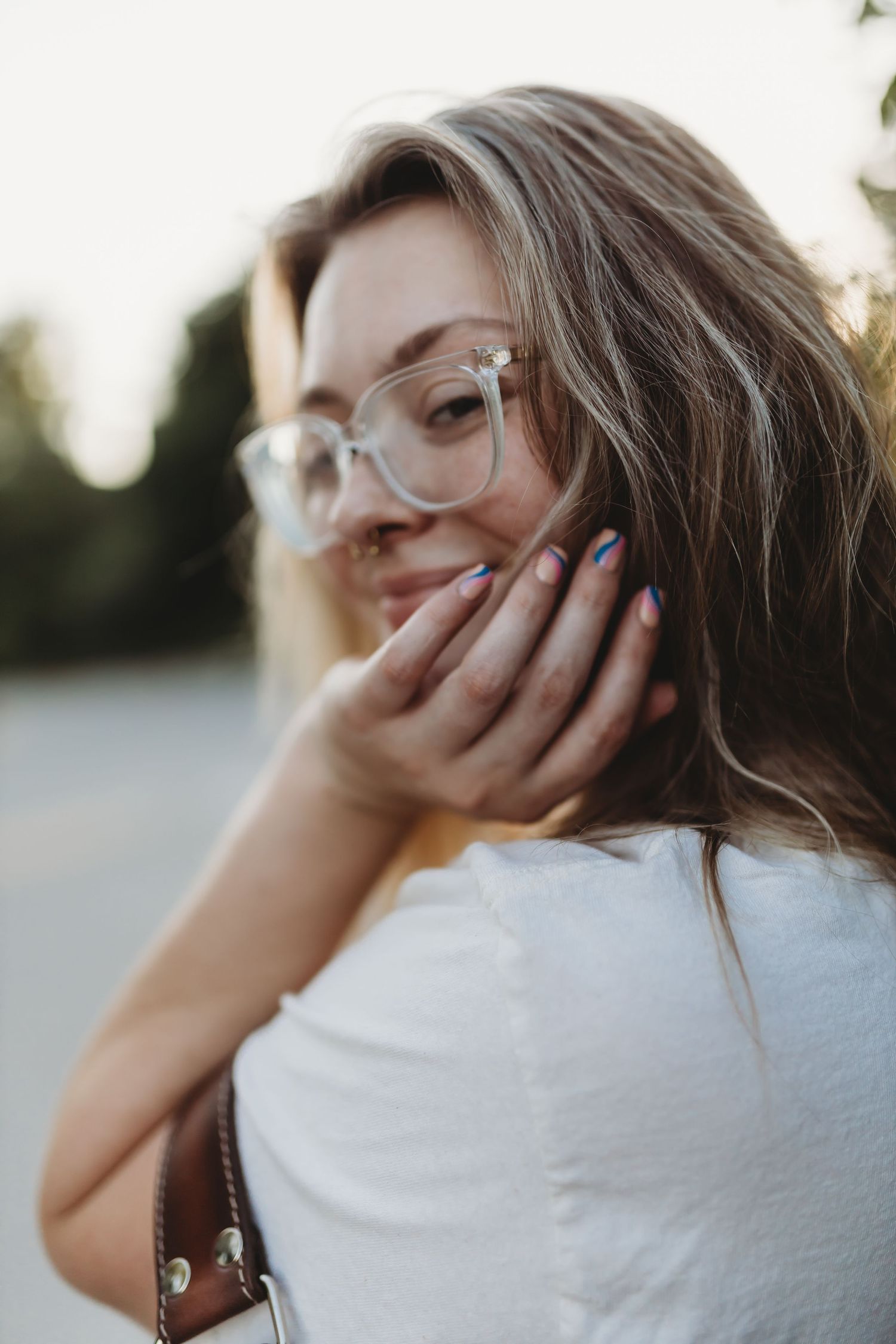 A candid portrait of someone with glasses laughing while covering their mouth.