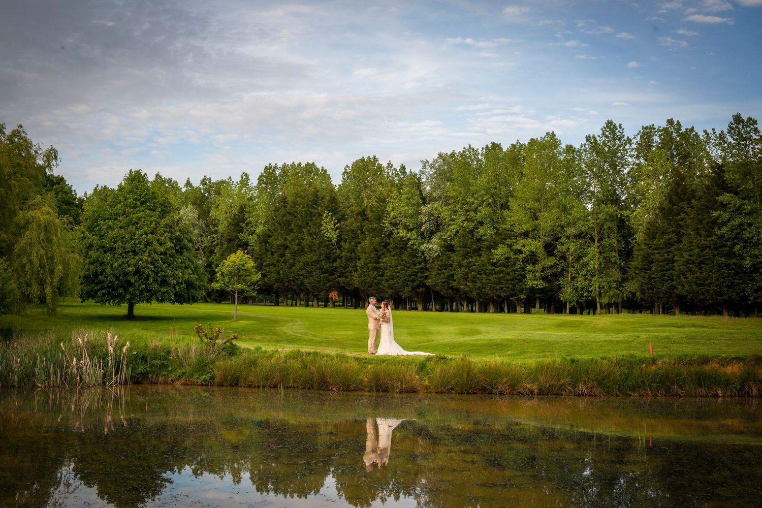 Panoramic view of a lakeside wedding venue with green trees and reflective water.