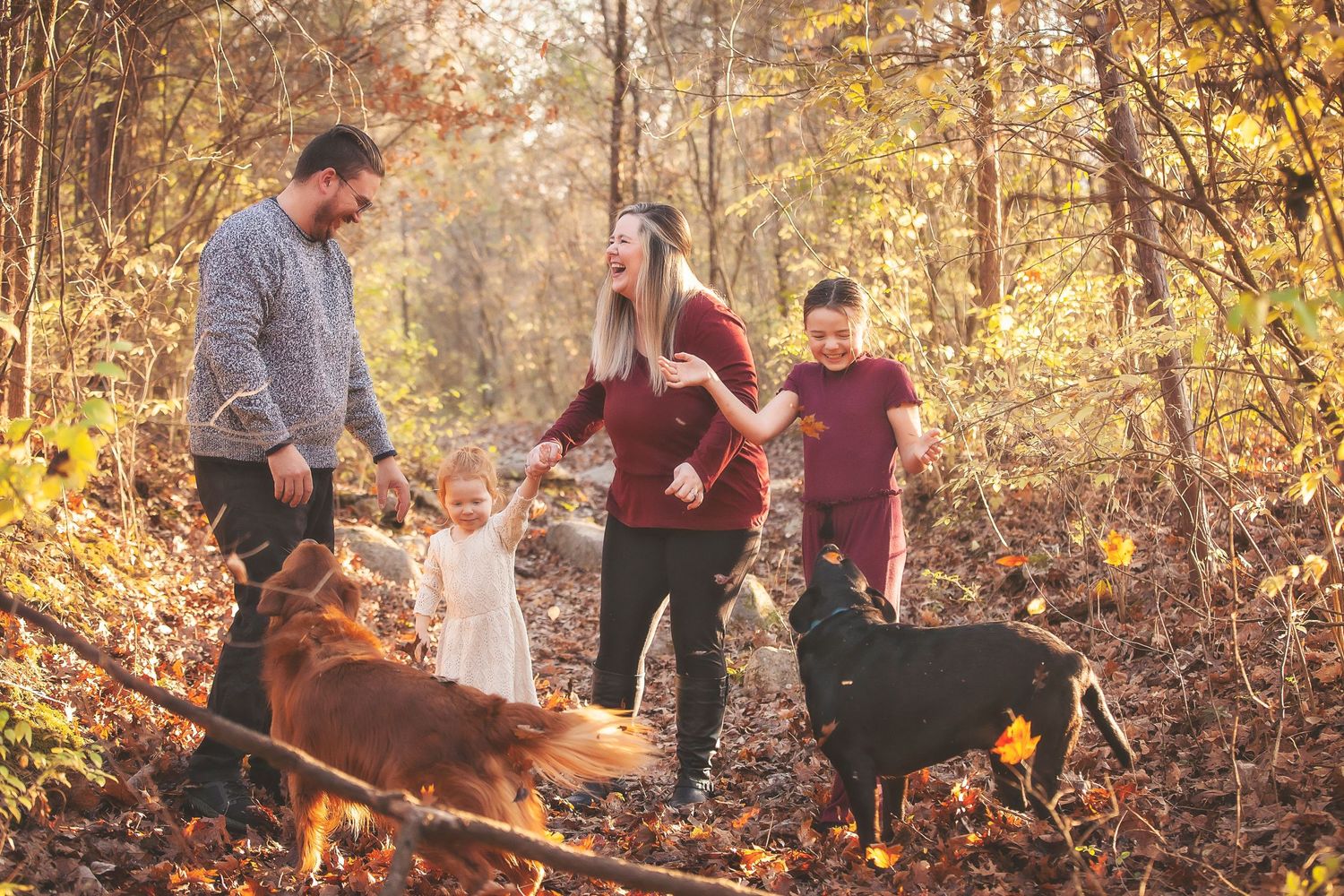 Happy family with two dogs playing in autumn forest with golden fallen leaves.