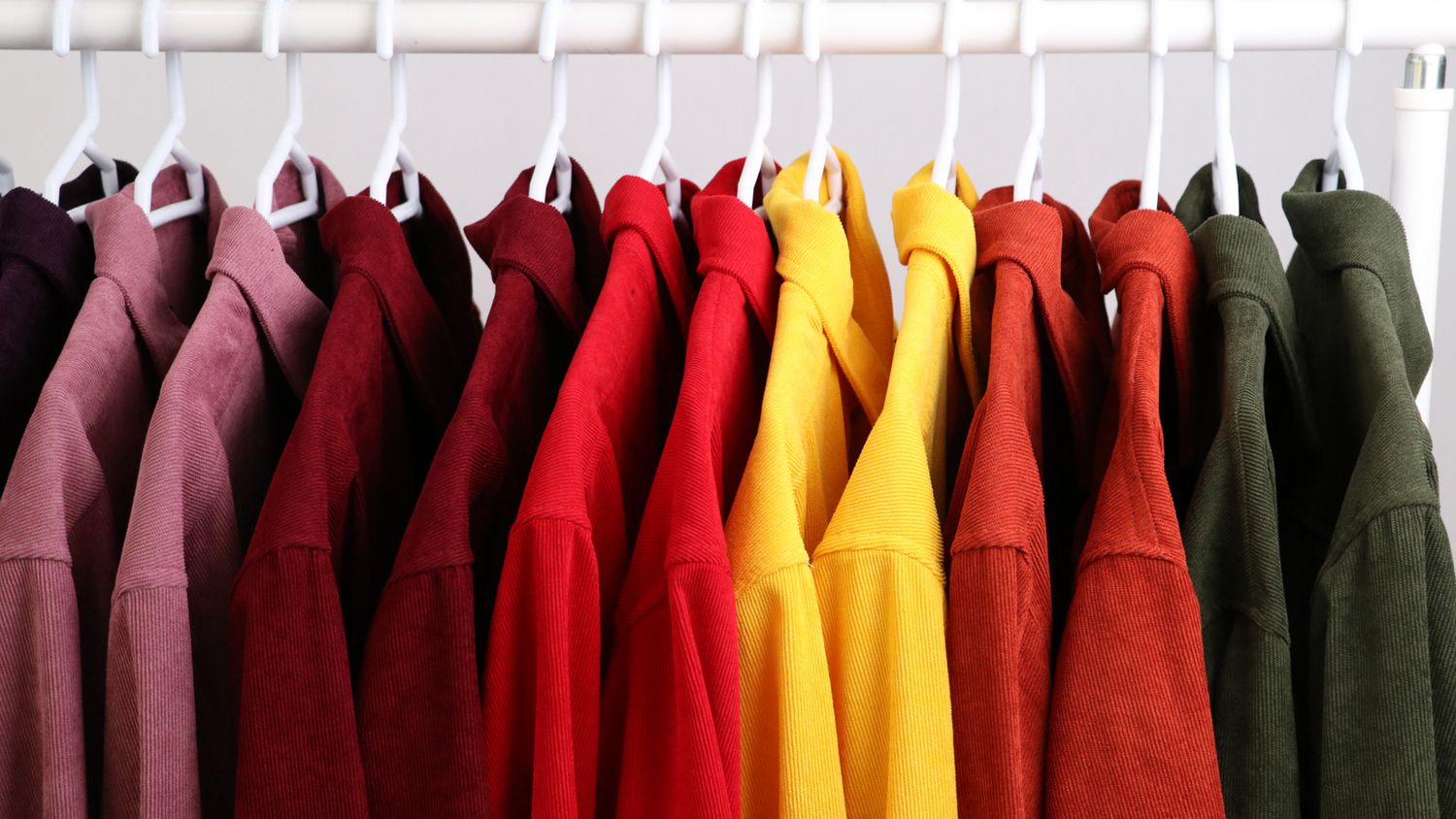 Row of colorful hooded sweatshirts hanging on rack from burgundy to yellow to green shades.