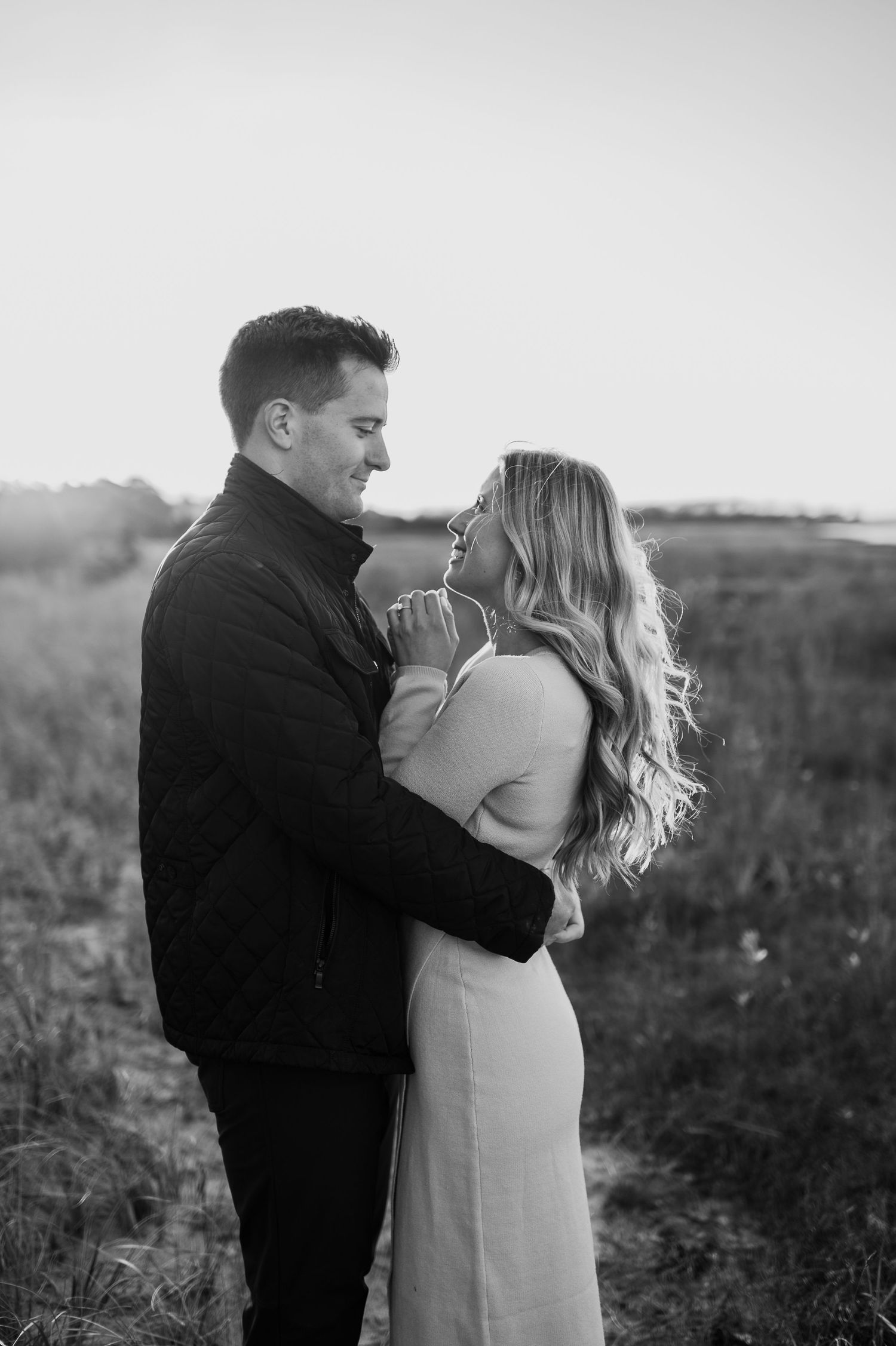 Black and white portrait of couple embracing in field at sunset.