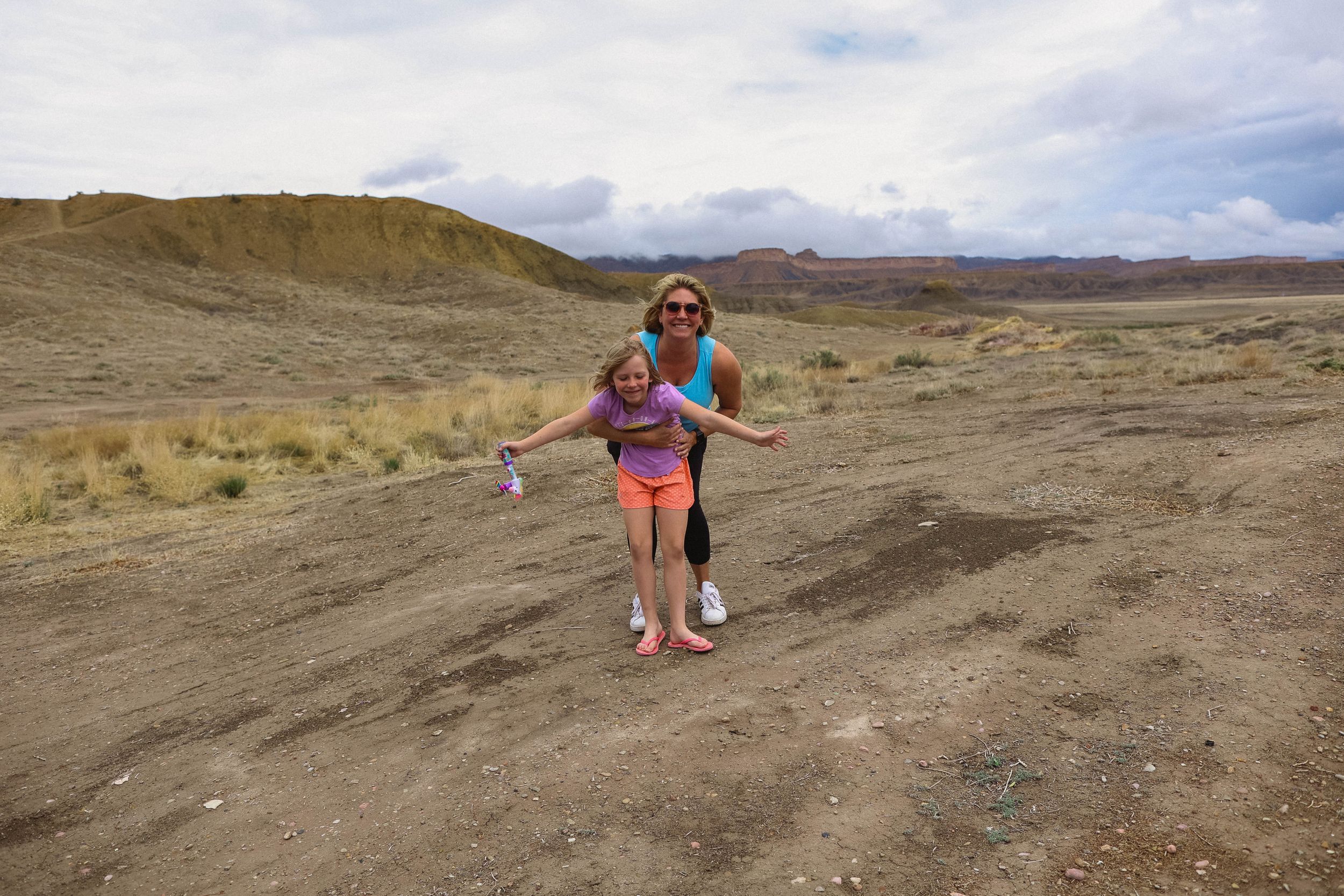 Desert hiking trail winds through arid terrain under partly cloudy skies.