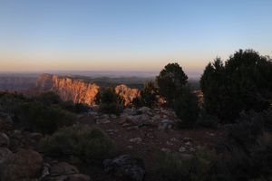 Panoramic view of desert cliffs glowing orange at sunset with dark silhouetted trees.