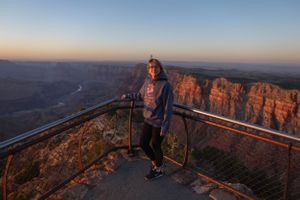 Tourists taking photos at canyon viewpoint with safety railing during sunset.
