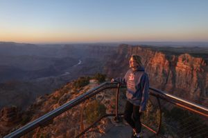 Panoramic view of the Grand Canyon's rocky cliffs and plateaus at sunset with observation deck railings visible.
