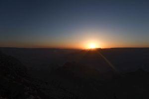 Dark silhouette of mountains against a dusky blue sky with the sun setting on the horizon.